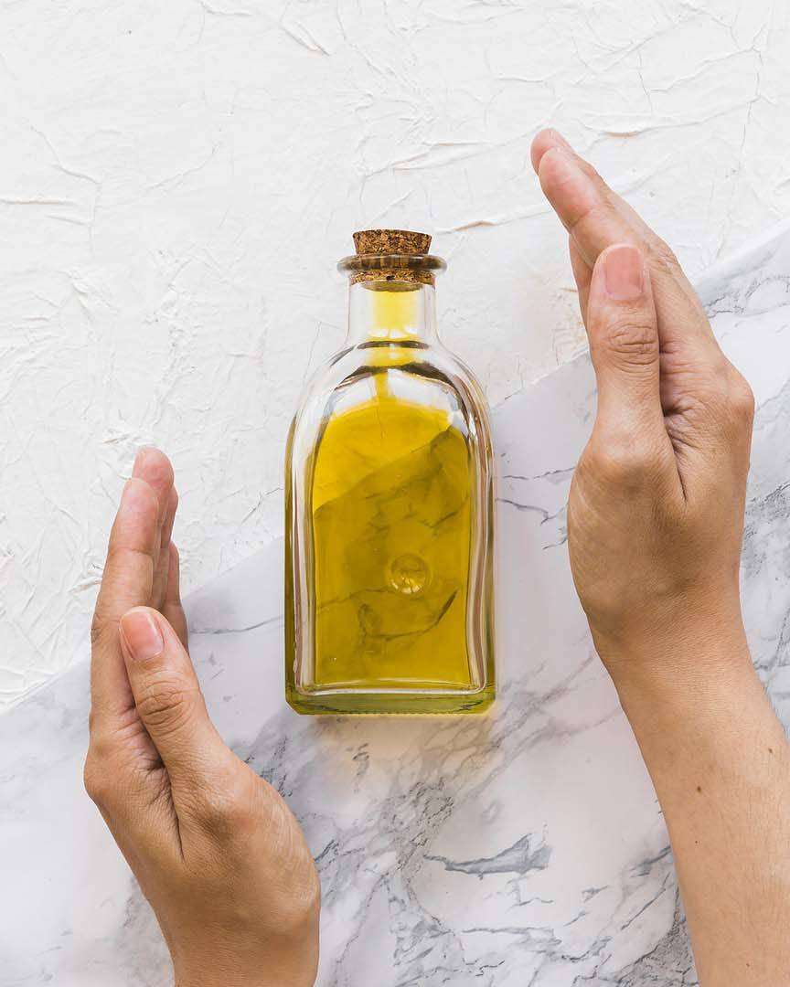 Olivenöl in kleiner Flasche, eingerahmt von Händen